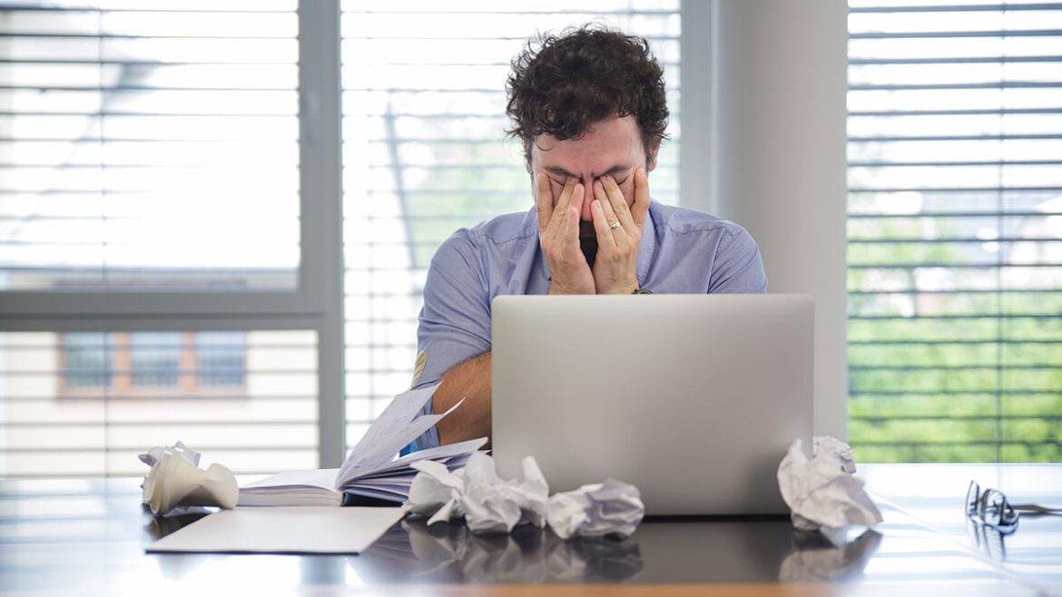 Un homme au bureau pose son visage dans ses mains en signe de fatigue.