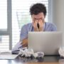 Un homme au bureau pose son visage dans ses mains en signe de fatigue.