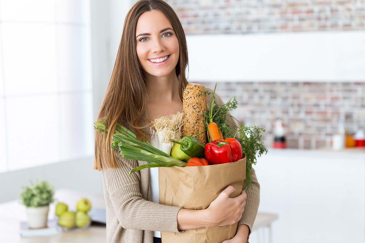 Une femme tenant dans ses bras un panier de légumes sources d'une alimentation saine.