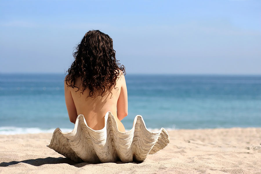 Femme sur une plage assise sur un coquillage.