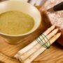 Un bol de velouté aux asperges avec des asperges épluchées sur la table.